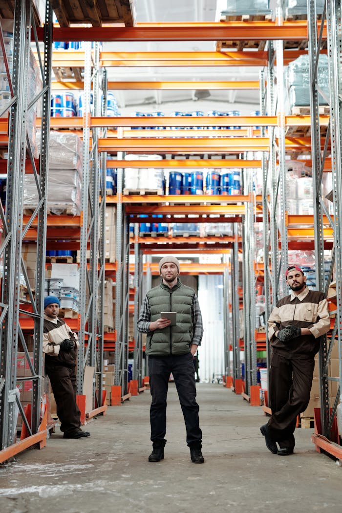 Three warehouse workers stand in an industrial aisle. Indoor workplace environment.