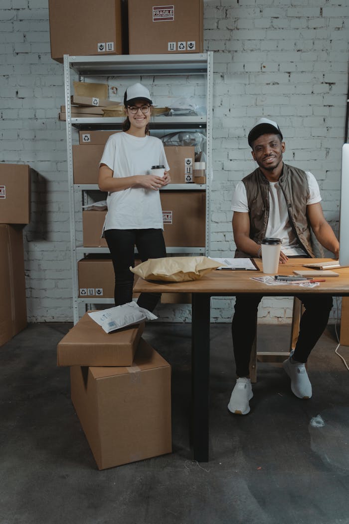 Two coworkers in a logistics setting surrounded by packages, smiling and working efficiently.